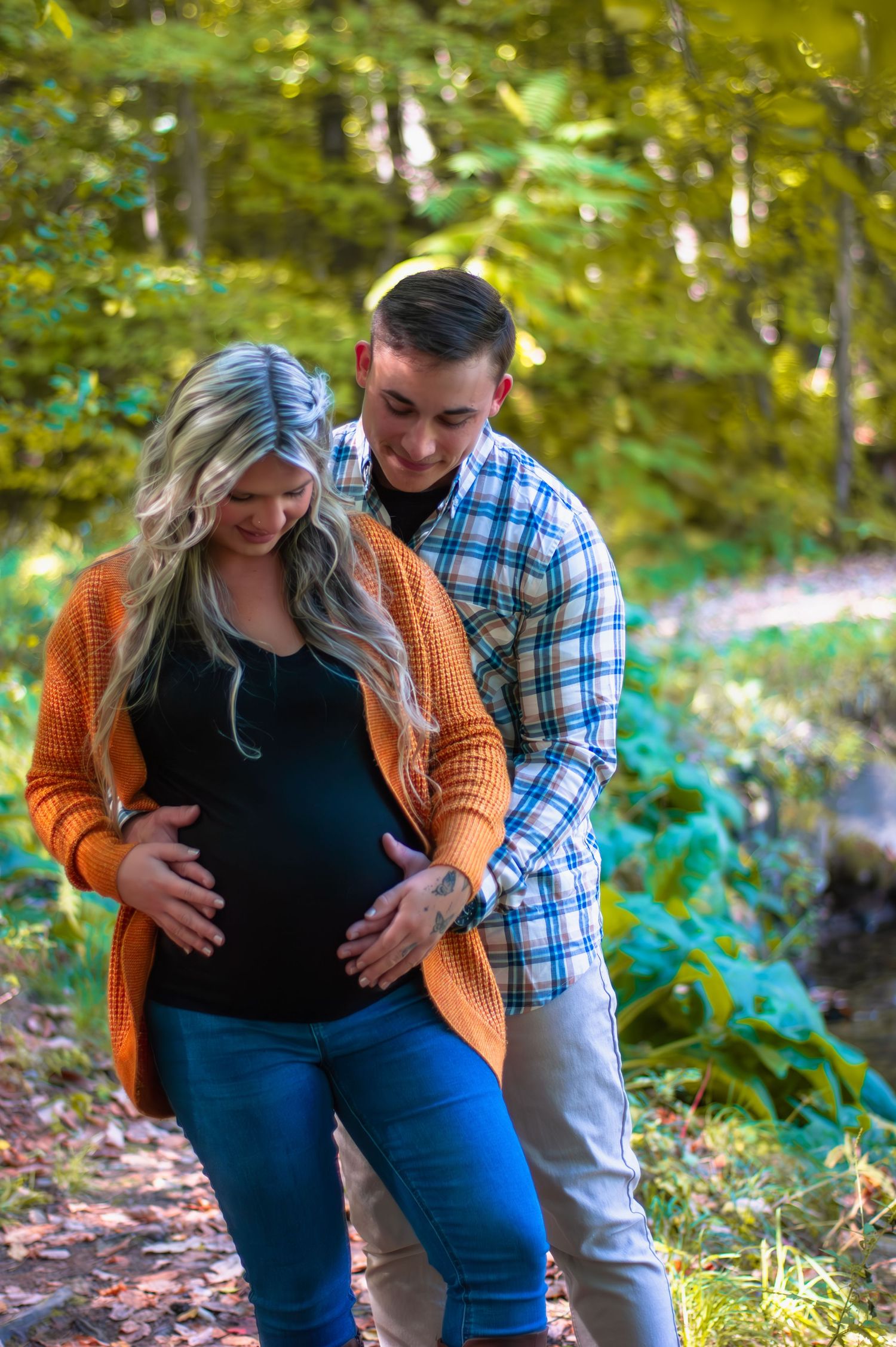 Expectant couple sharing intimate moment on autumn trail with stream in background.