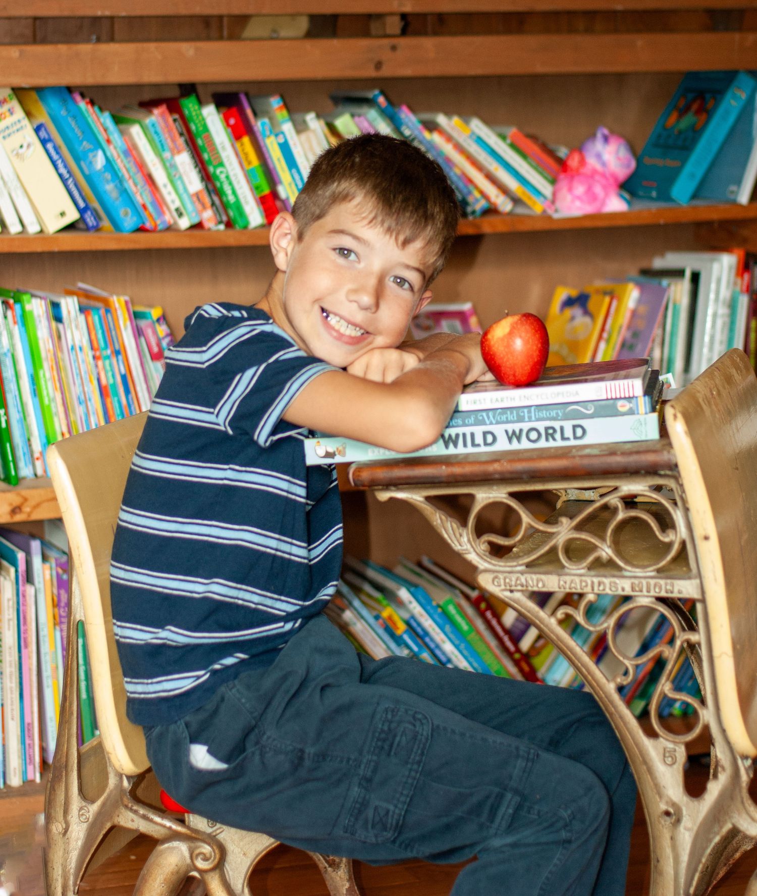 A child relaxes in a cozy reading nook surrounded by colorful books on wooden shelves.