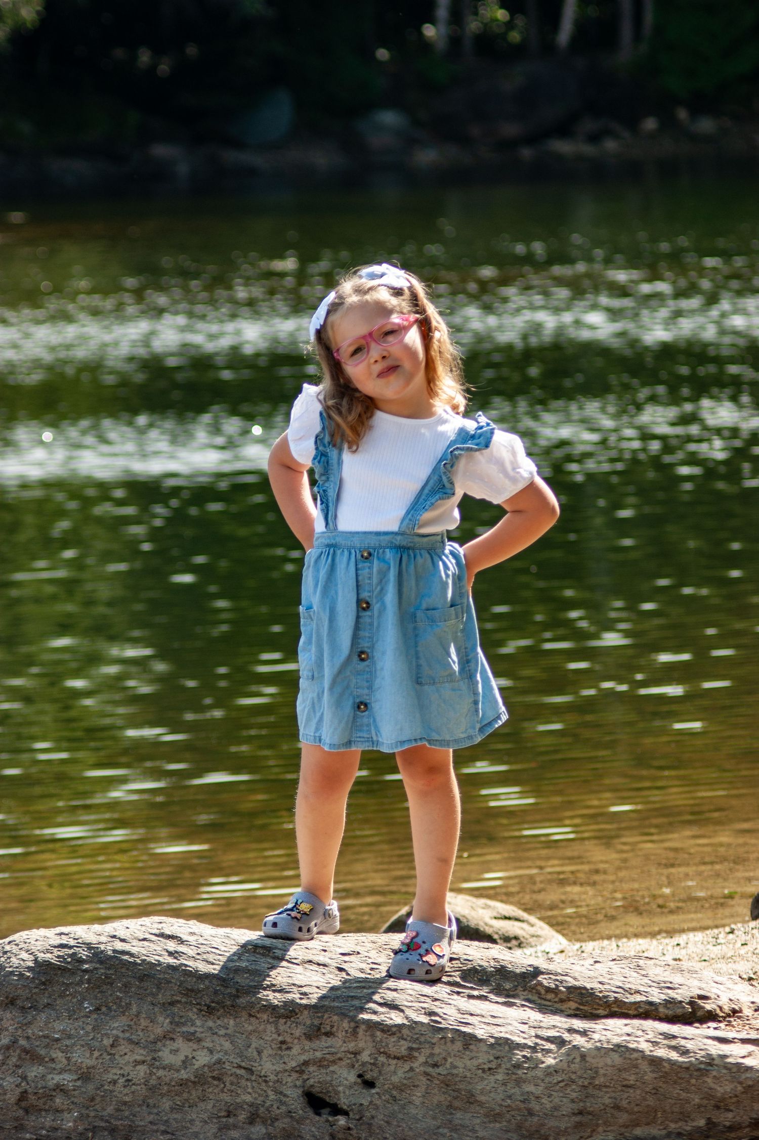 A cheerful child poses confidently on a rock by a tranquil lake
