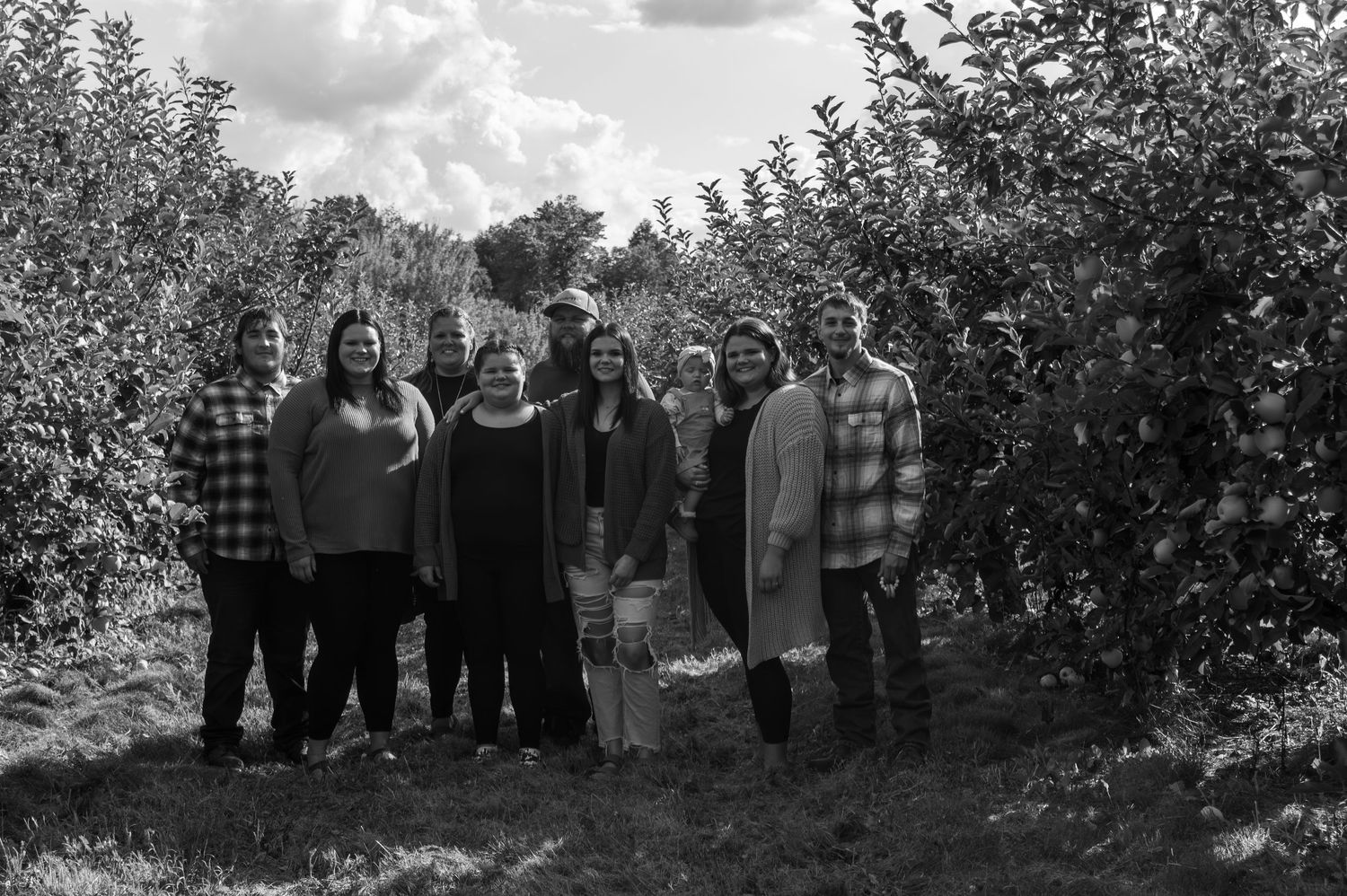 A group of people stand together between rows of fruit trees in an orchard.
