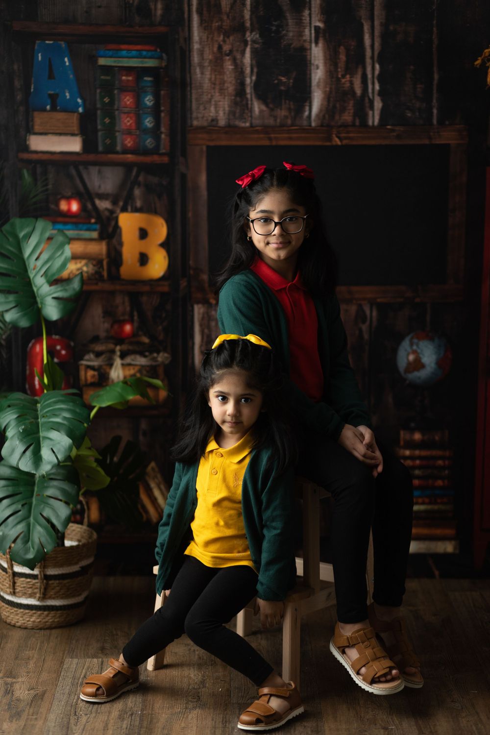 Two students in colorful outfits posing on chair against rustic classroom setting with decorative letters.