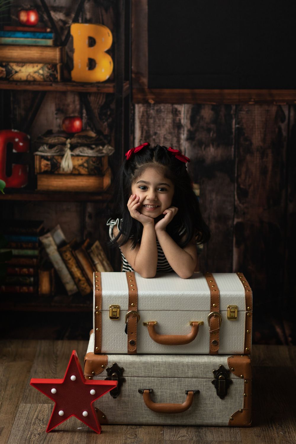Child posing with vintage suitcases and star decoration against rustic backdrop with decorative letters.
