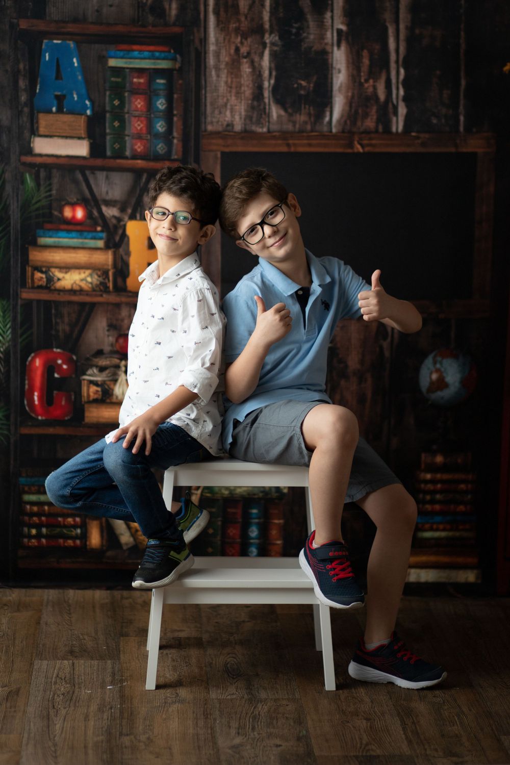 Two students posing together on white chair against vintage classroom backdrop with decorative letters.