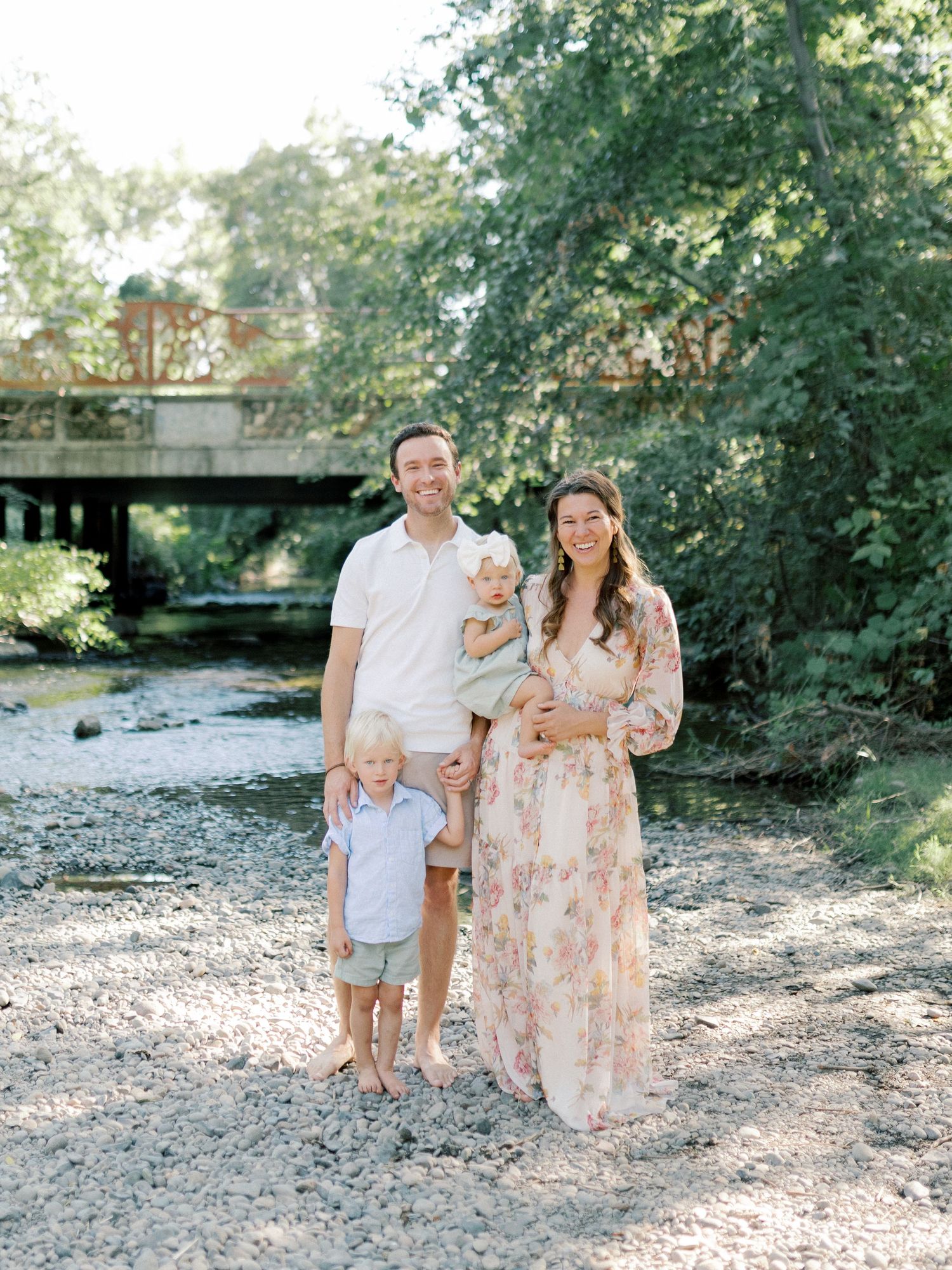 A joyful family of four posing creekside in Chico, CA captured by Kaitlin Stoltenberg in a natural-light session.