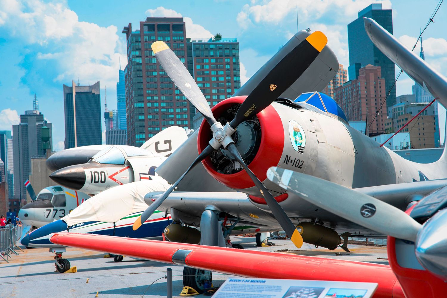 A vintage propeller aircraft with US military markings on display with city buildings in background.