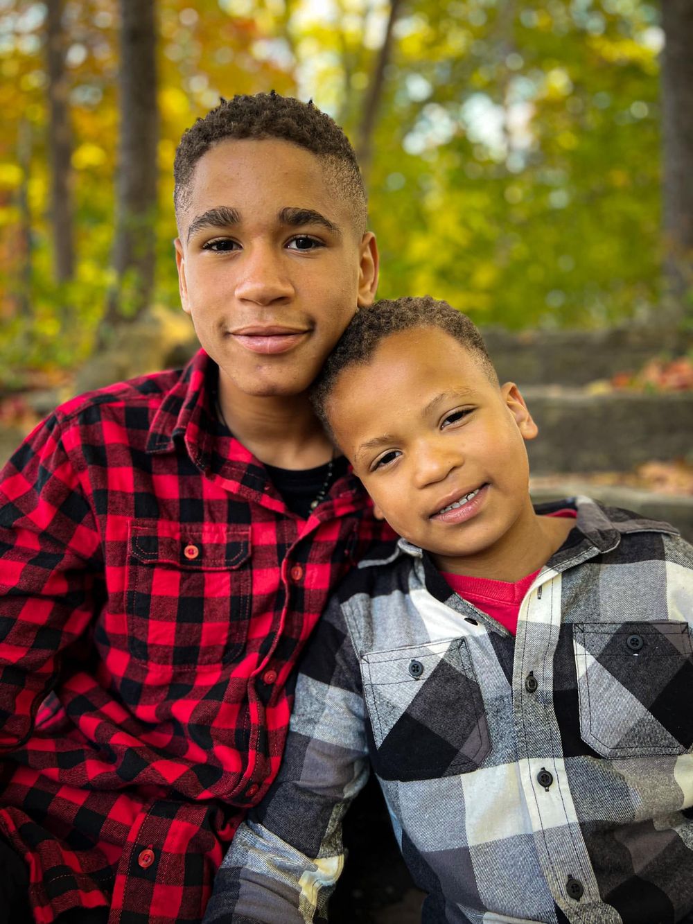 Two people in plaid shirts share a warm moment outdoors with fall foliage in the background.