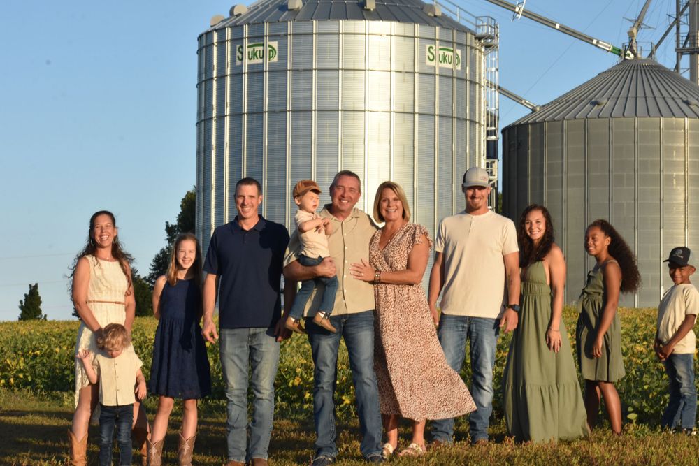 Family group poses together at sunset in front of large grain silos on farm.
