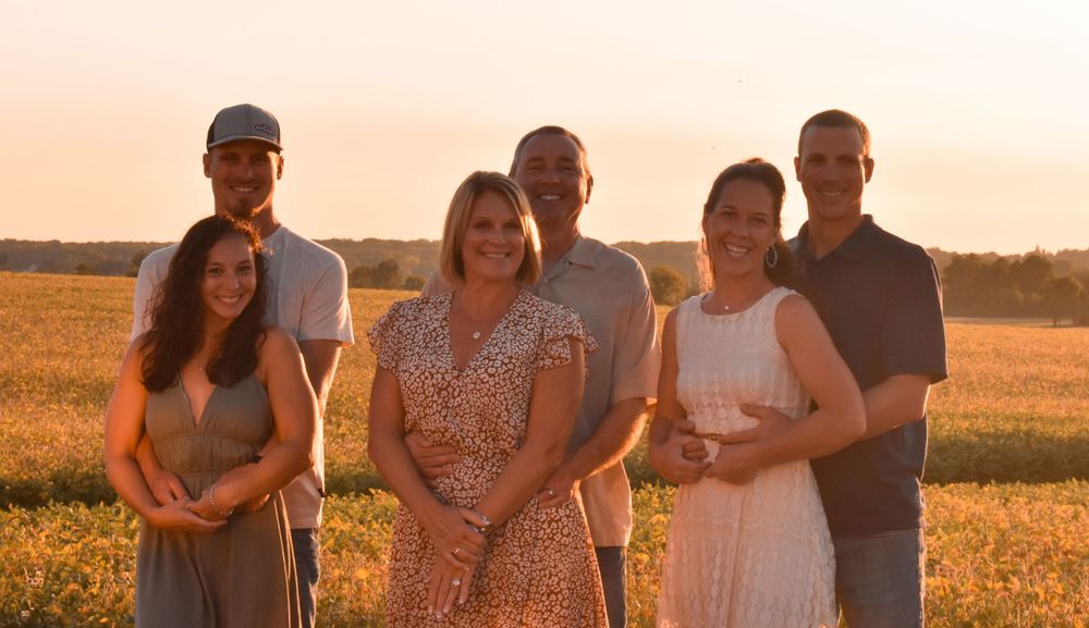 Group of people pose together in field during golden hour sunset.