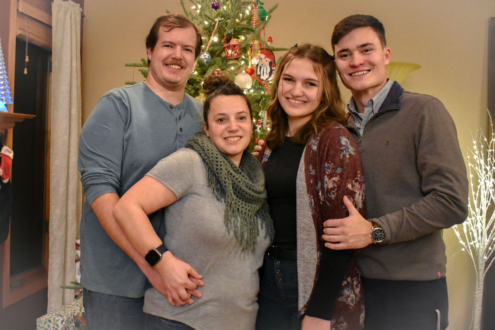 A group poses together in front of a decorated Christmas tree in a warm indoor setting.