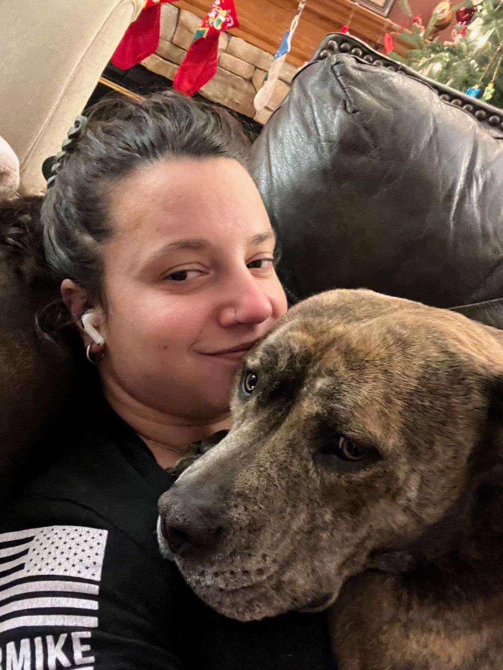 Close-up selfie of person cuddling with brindle pit bull type dog on leather couch.