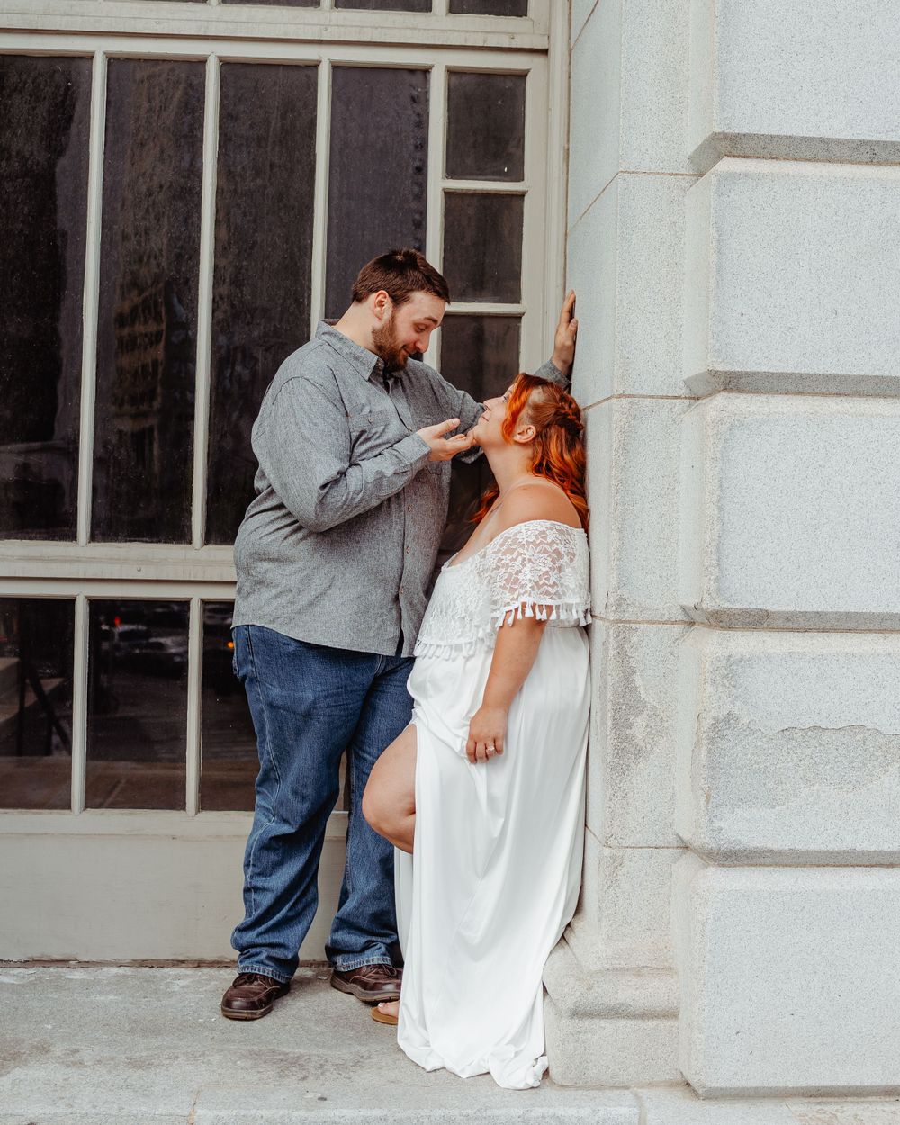Romantic wedding moment captured against a white stone building wall.