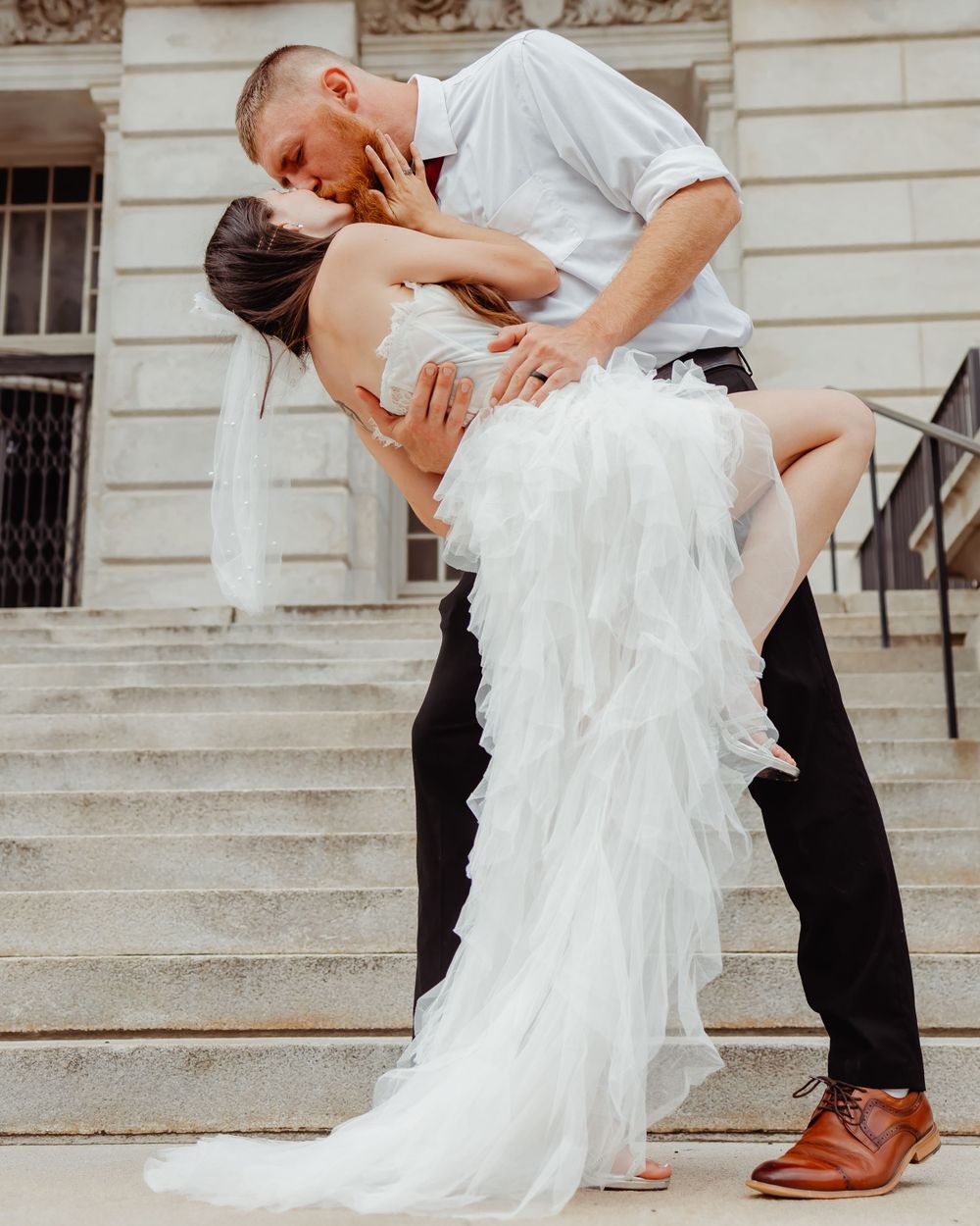 Dramatic wedding dip pose on stone steps with flowing white dress.
