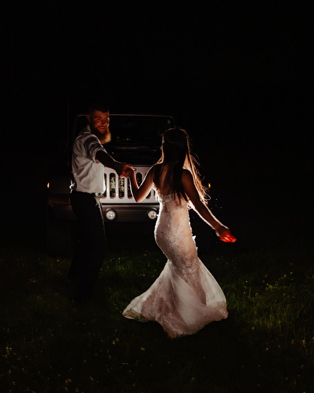 Dramatic night wedding photo with vintage car headlights illuminating a flowing white dress.