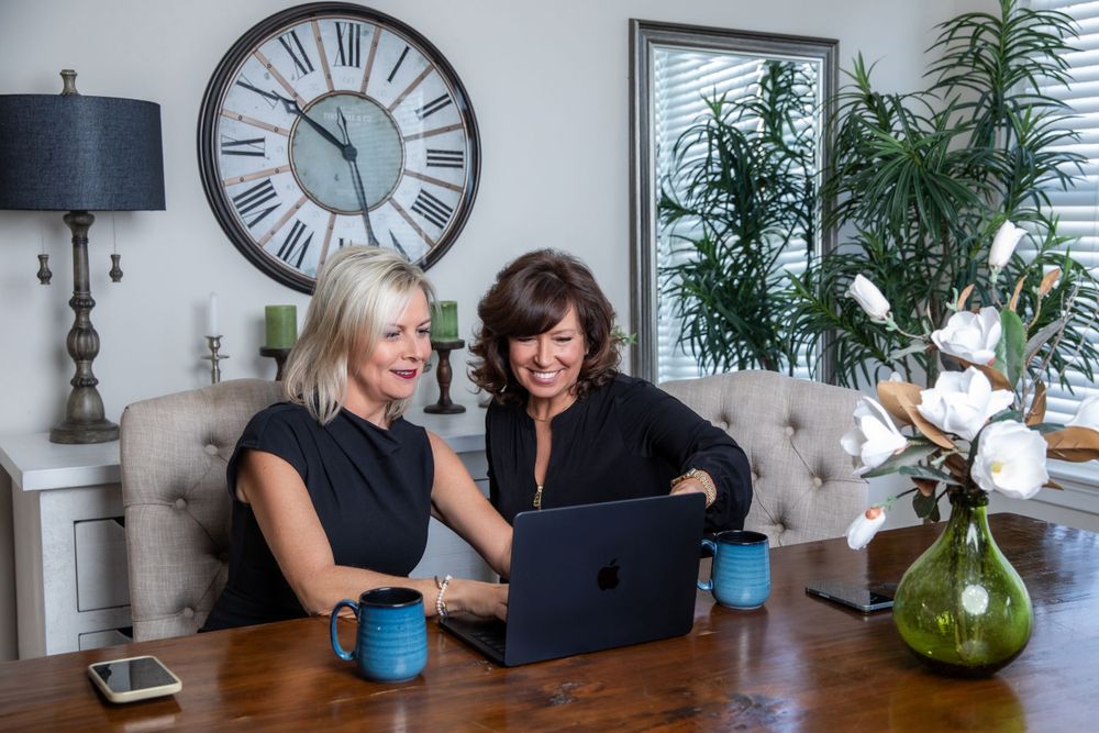 Two people collaborating while looking at laptop in bright home office environment.