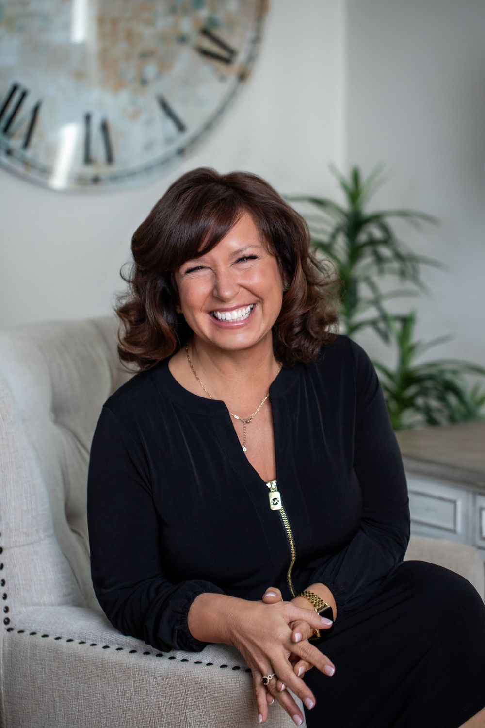 Person in black outfit sits comfortably in gray armchair with modern decor.
