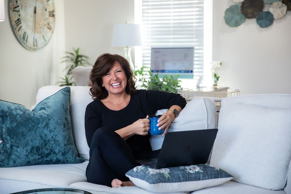 Person relaxing on teal velvet couch with laptop in modern living room setting.