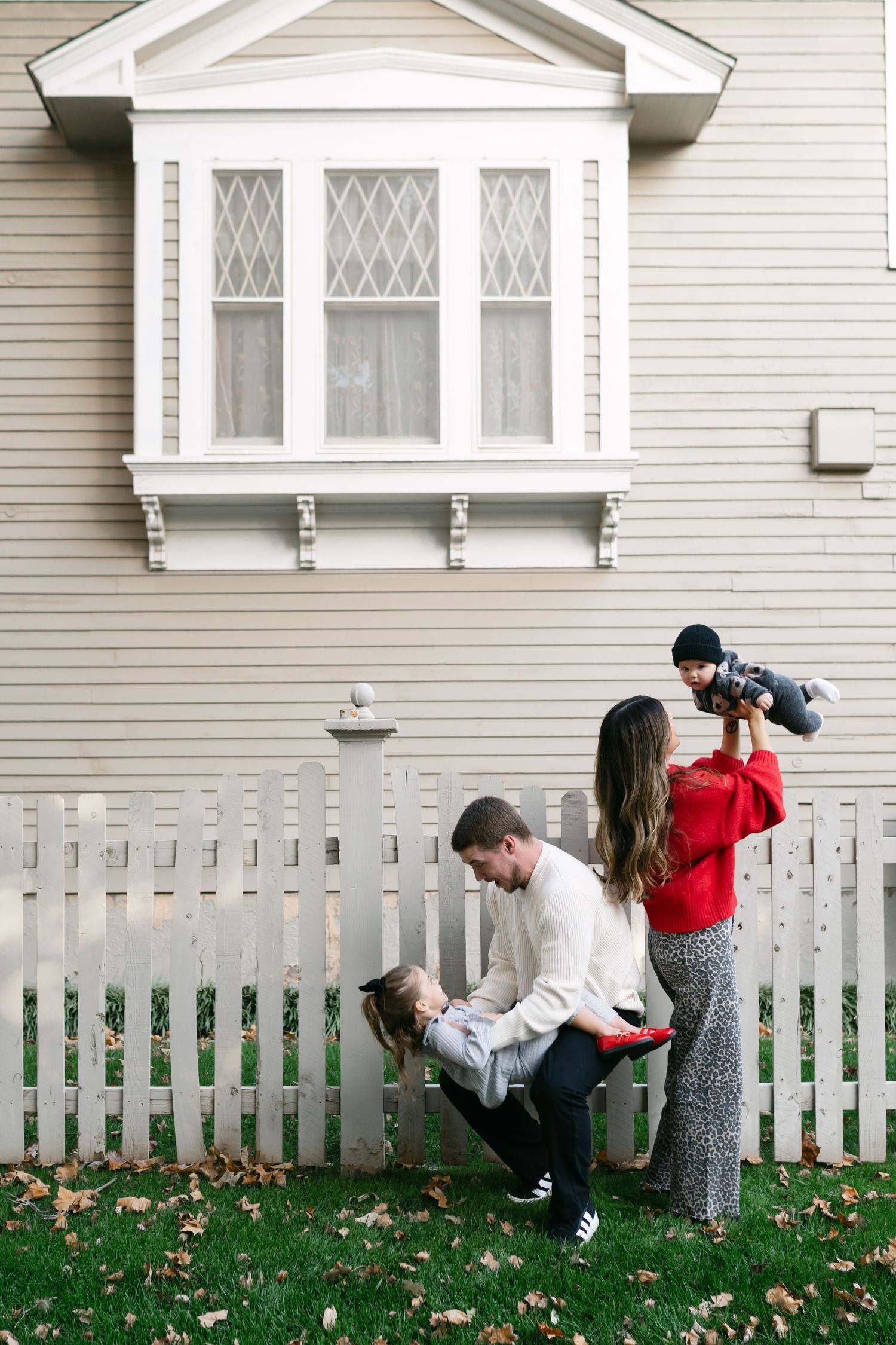 Playful family moments captured in sequence against white house and picket fence.