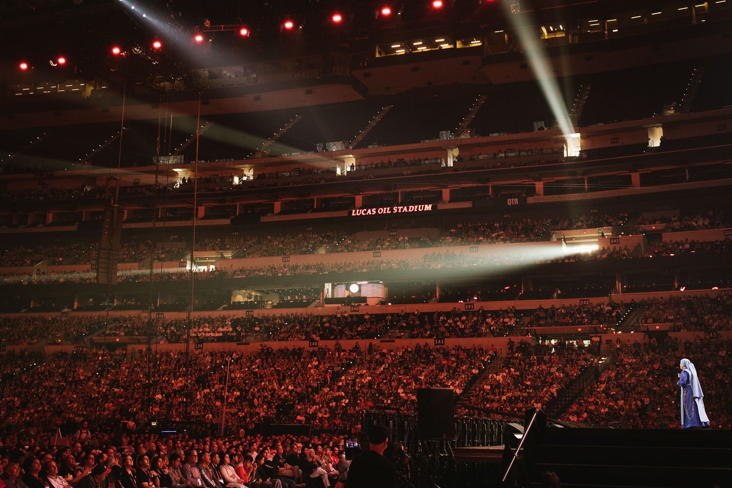Large arena concert venue with dramatic lighting and packed crowd.