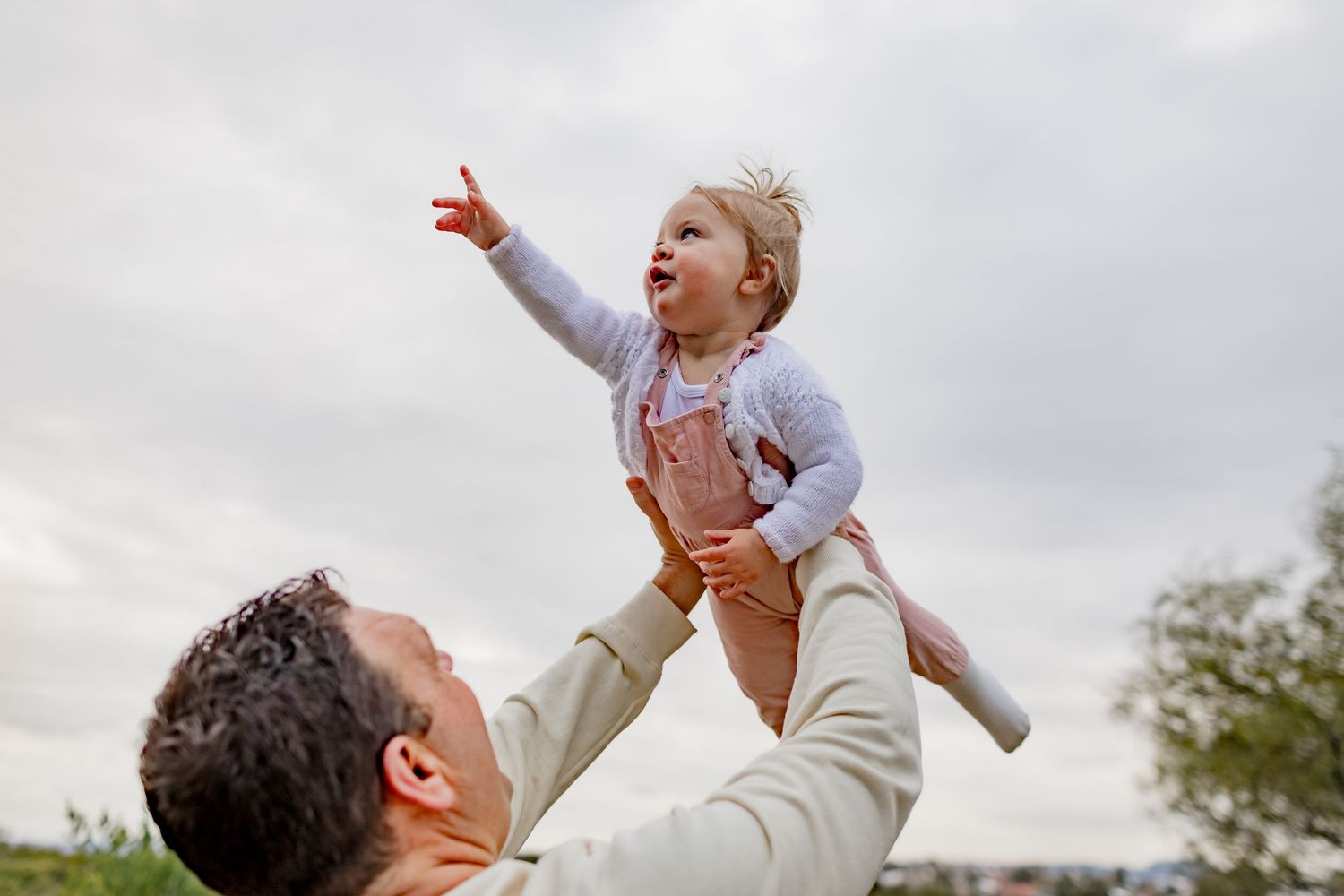 Joyful moment captured as parent lifts child high in the air against cloudy sky.