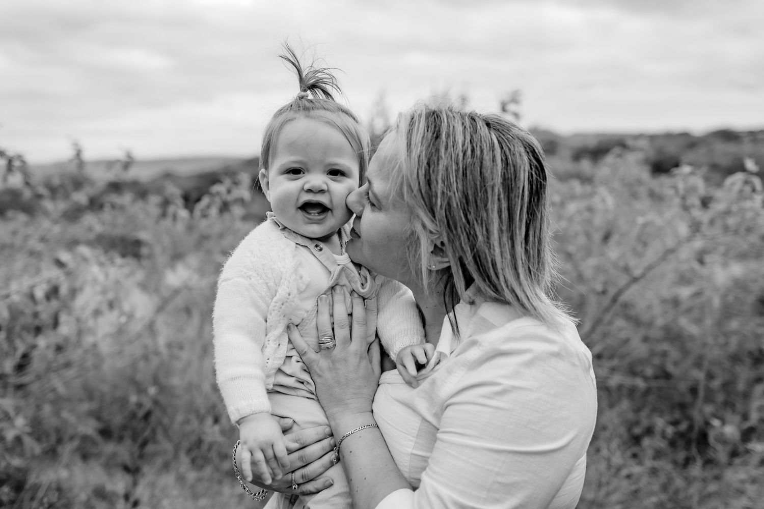 Black and white portrait of tender moment between parent and baby outdoors.