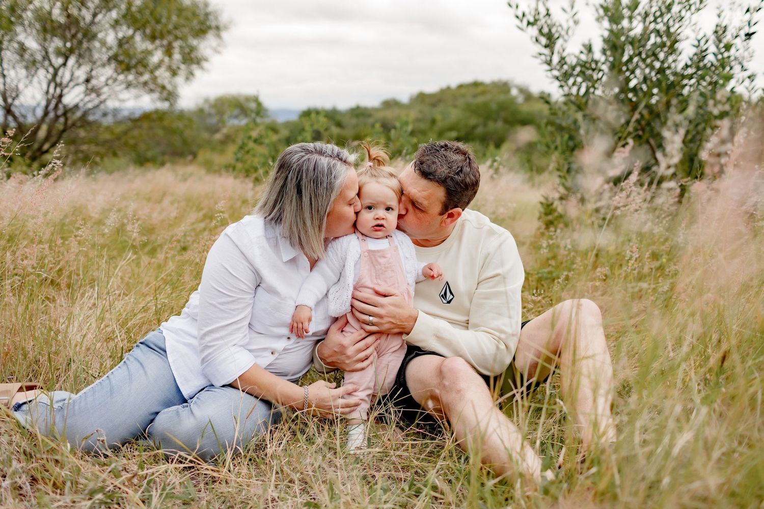 Intimate family moment captured in outdoor setting with tall grass and natural lighting.
