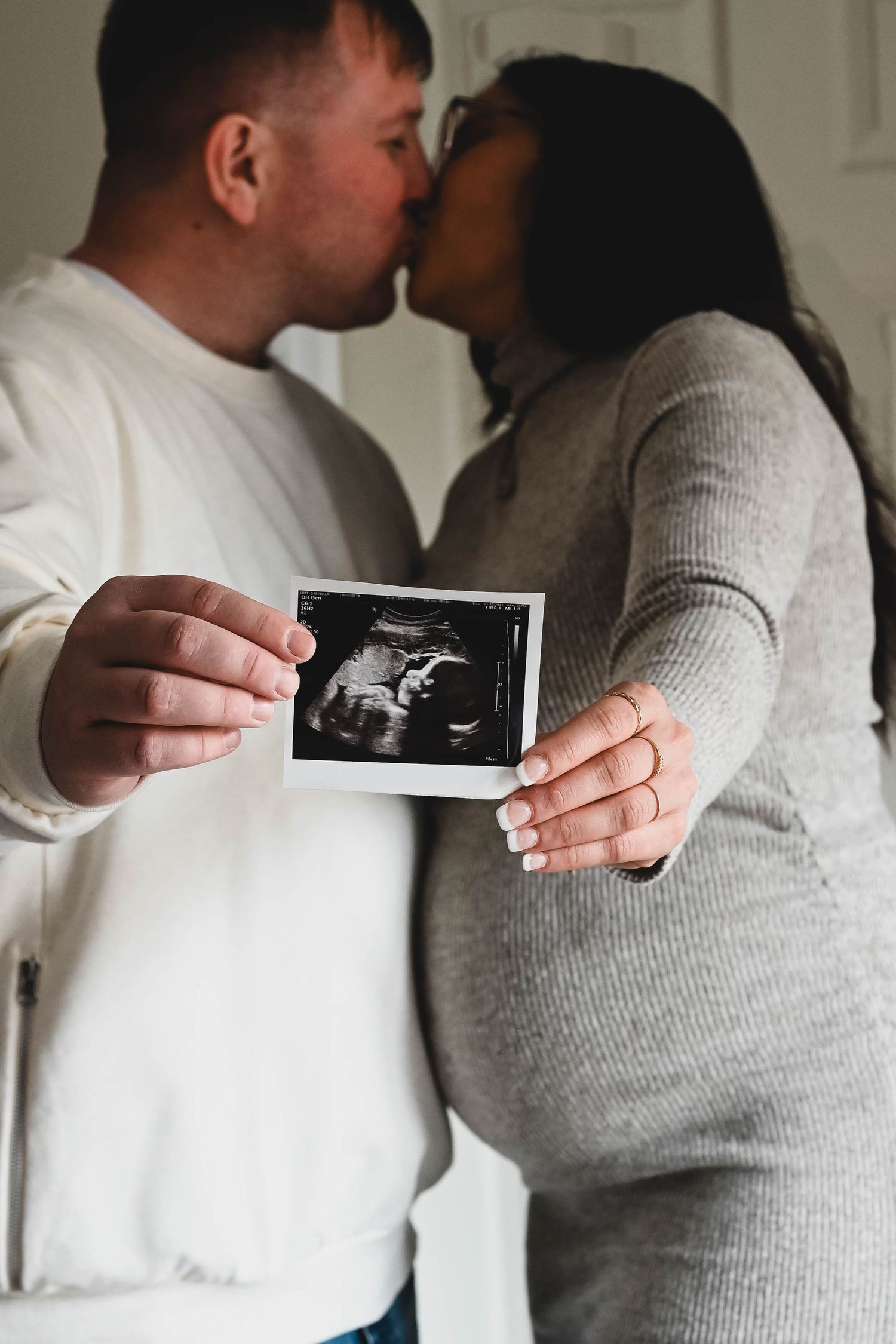 Mom and Dad share a kiss while holding ultrasound photo in maternity session in Albany, NY