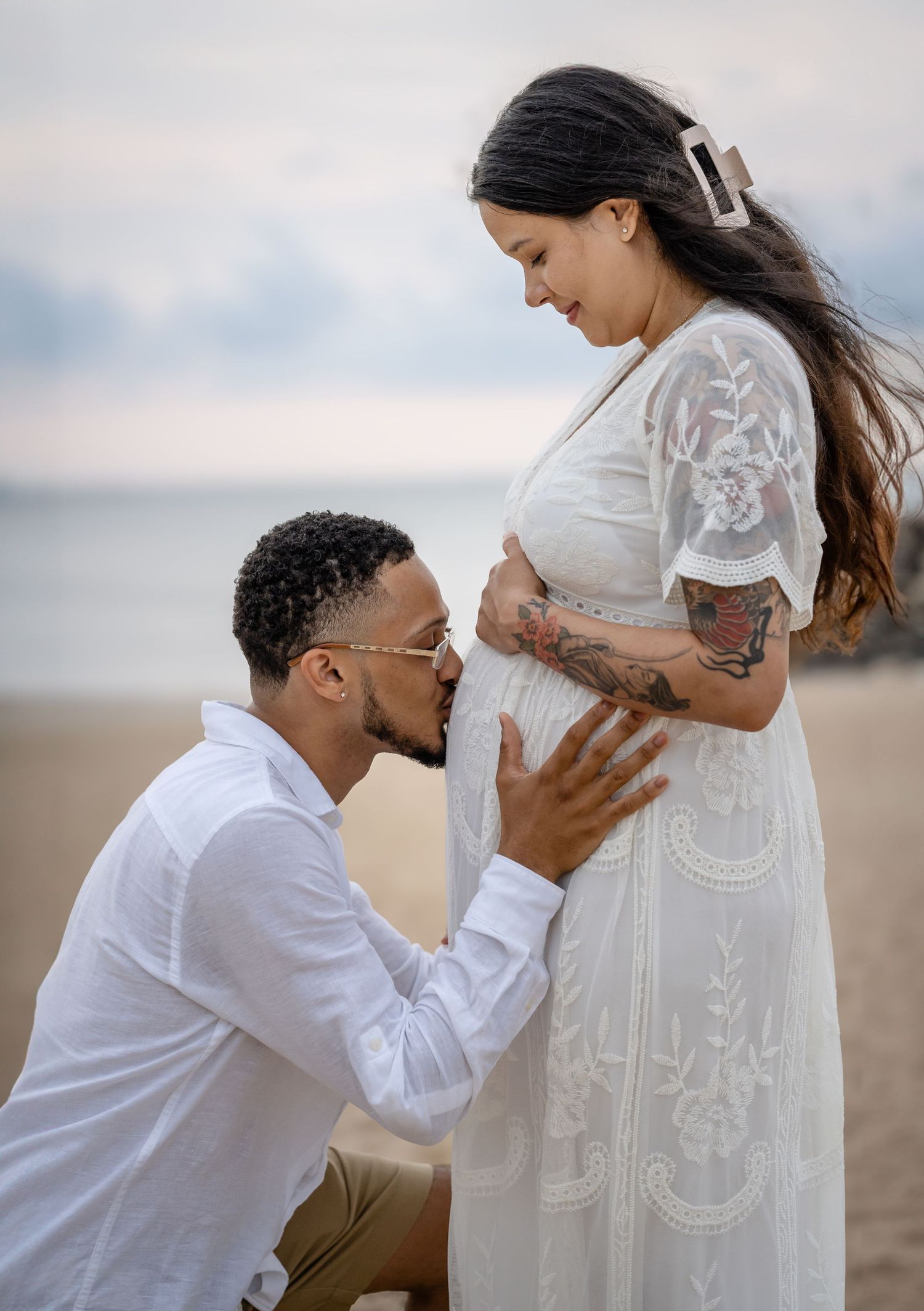 Expectant couple shares an intimate moment on the beach as partner lovingly touches pregnant belly.