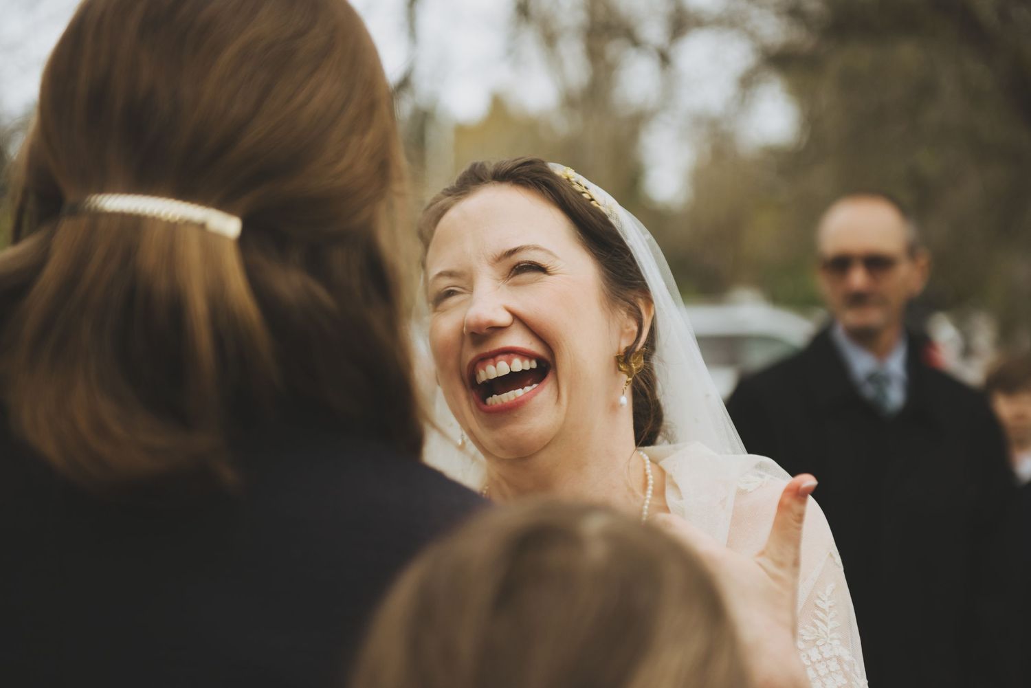 Bride laughing joyfully during outdoor wedding reception with guests.