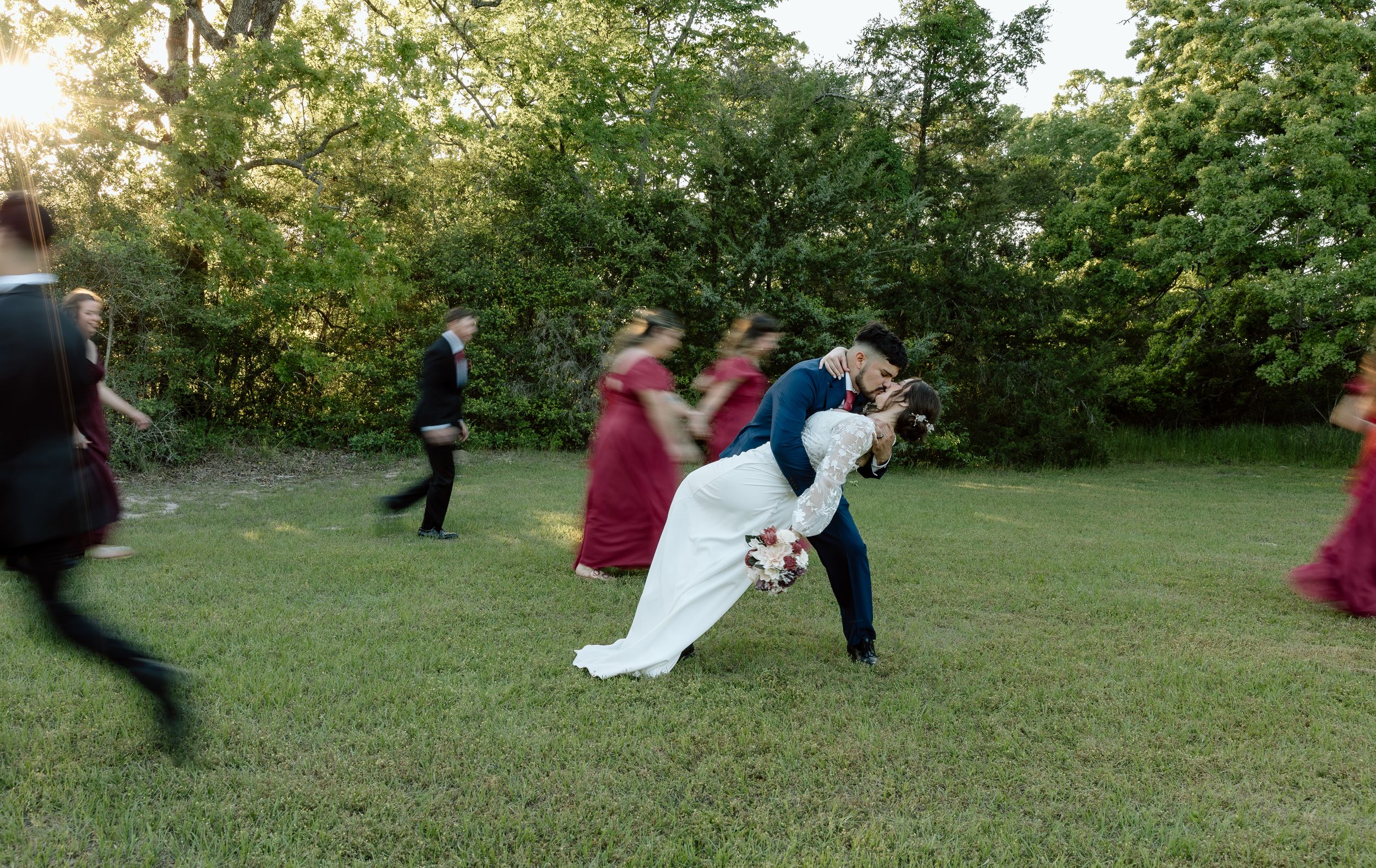 Dancing couple performs a dramatic dip move on a grassy lawn during an outdoor celebration with onlookers.