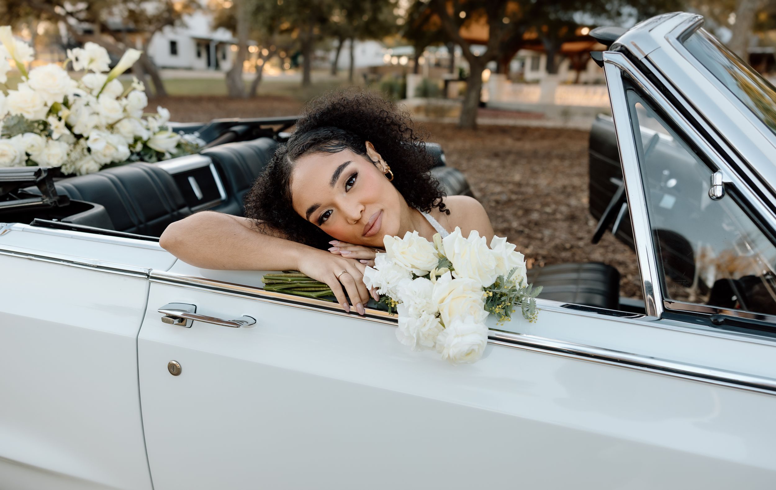 A vintage white convertible car decorated with white flowers parked in an outdoor setting.