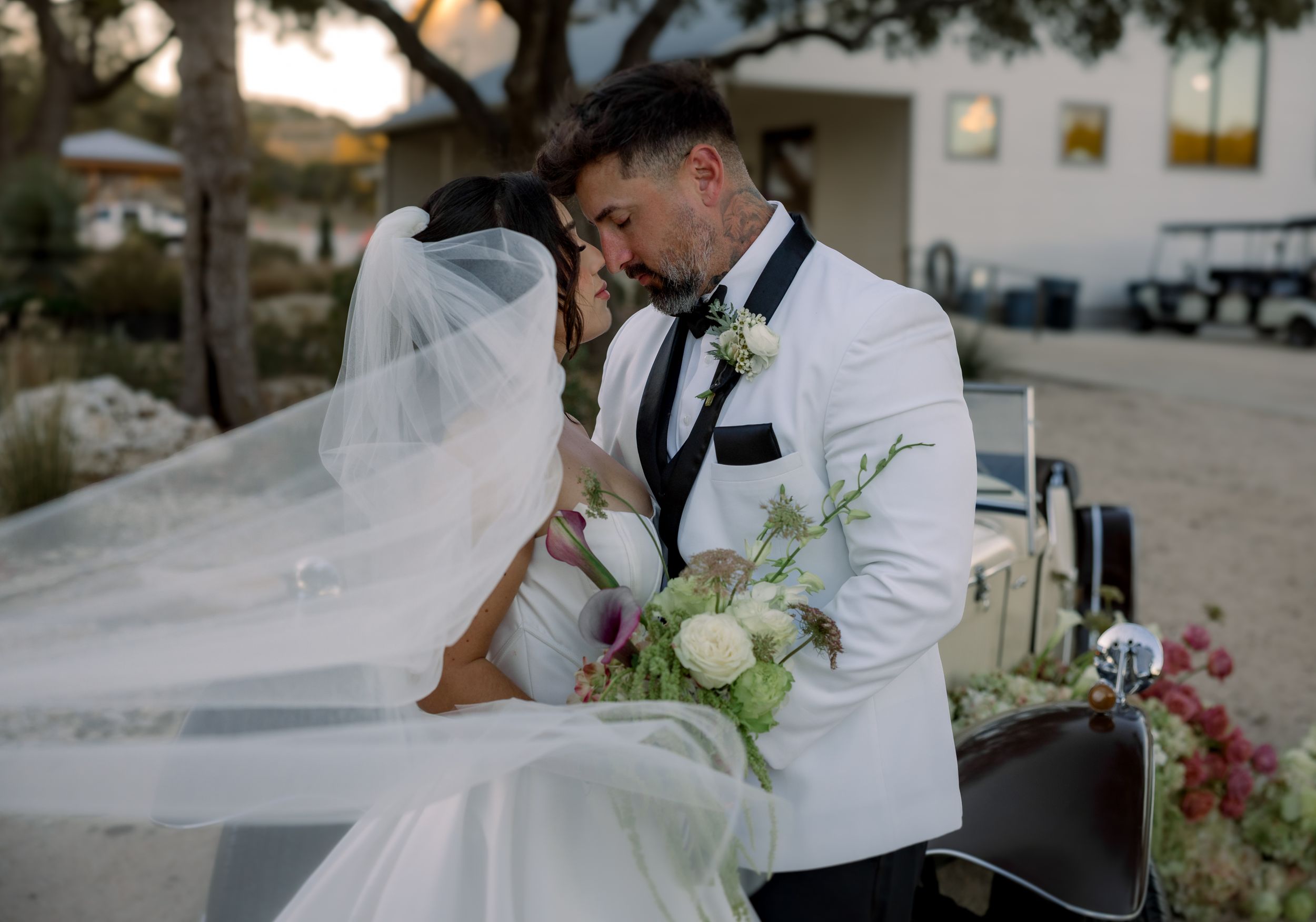 A romantic wedding moment captured outdoors with a flowing veil and white bouquet at golden hour.