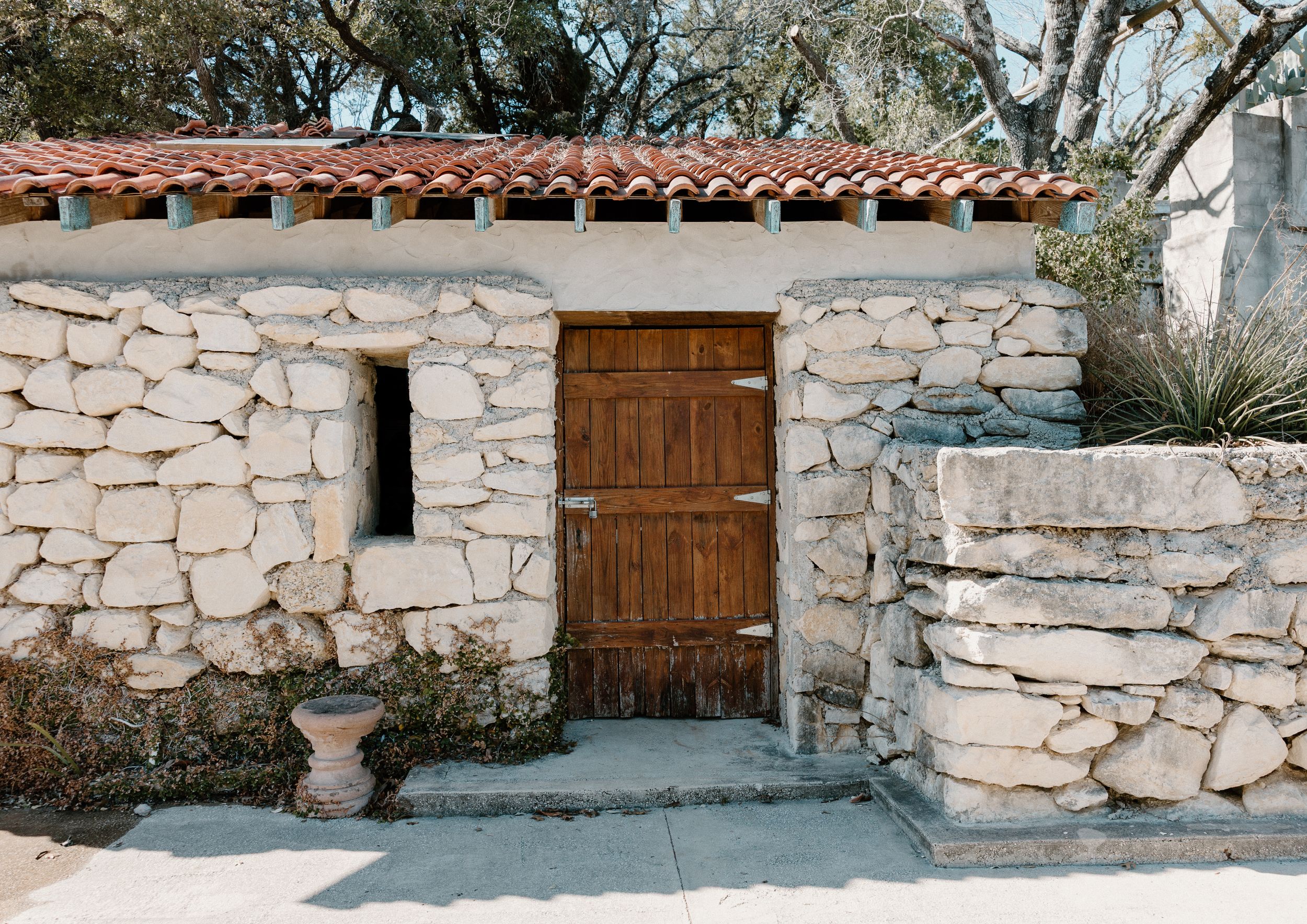 Rustic stone building with wooden door and terracotta tile roof in Mediterranean architectural style.