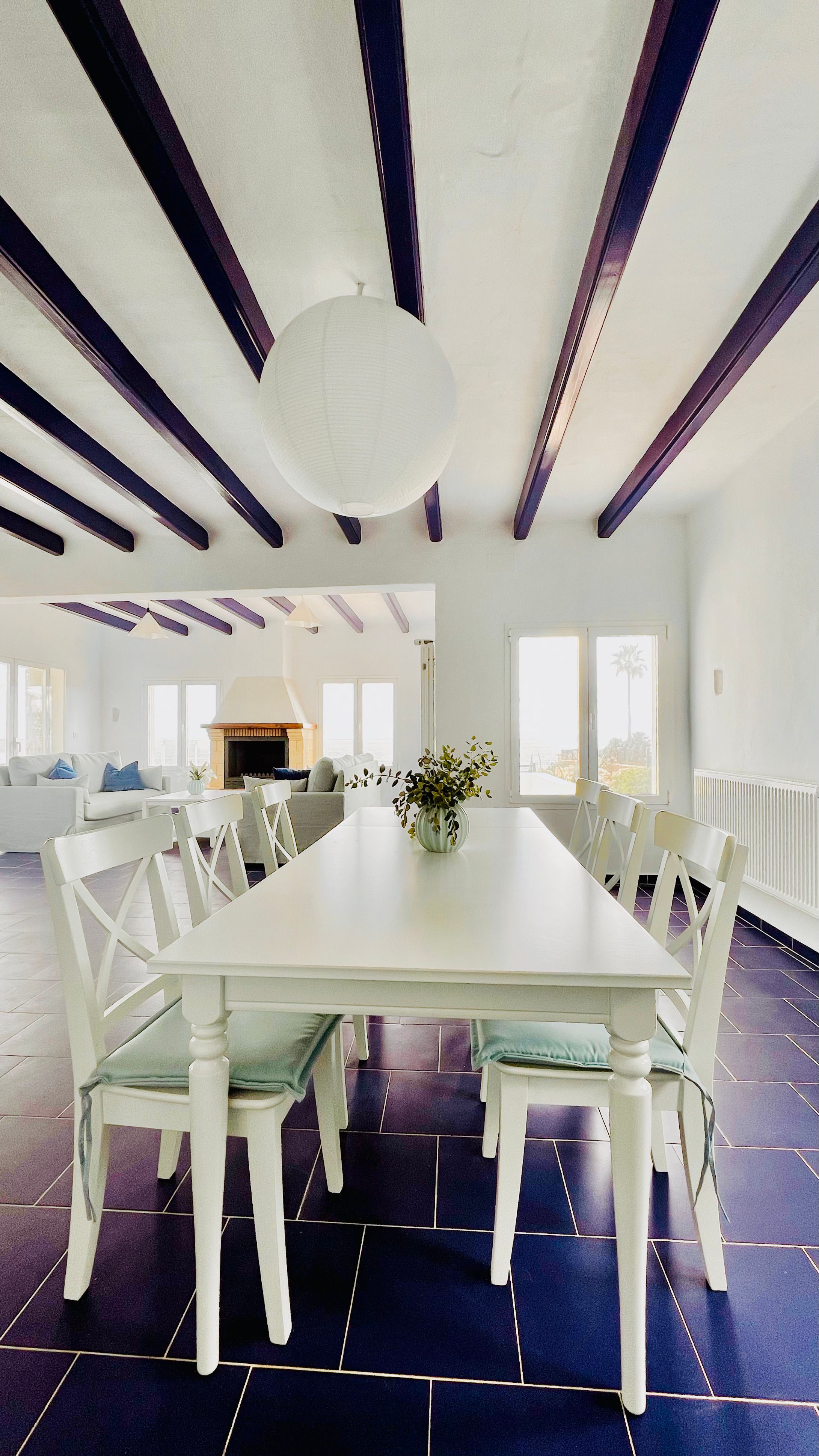 Modern dining room with white tables and chairs features exposed black ceiling beams and sleek dark flooring.