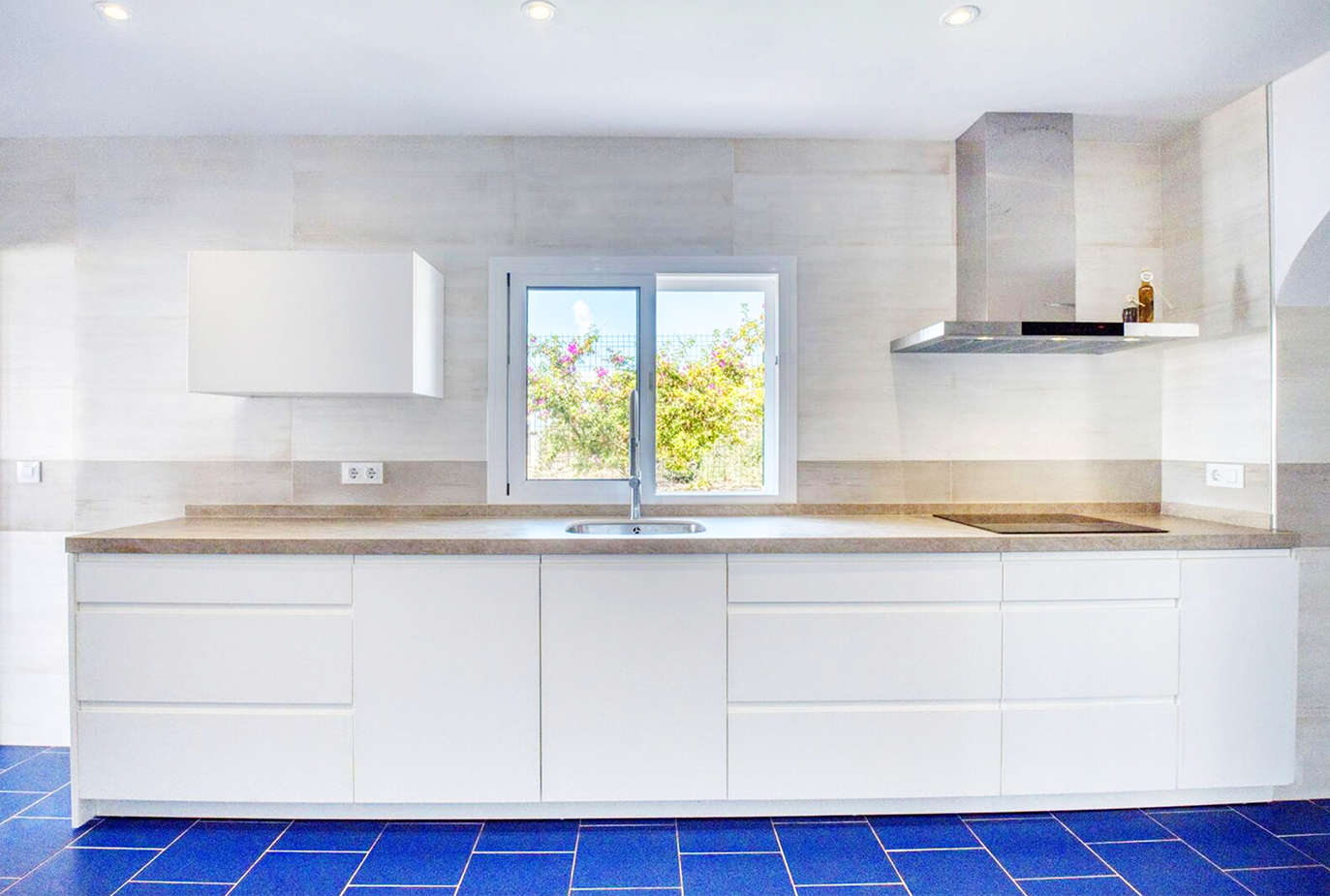 Modern white kitchen with blue tile floor and wooden countertops overlooking garden window.