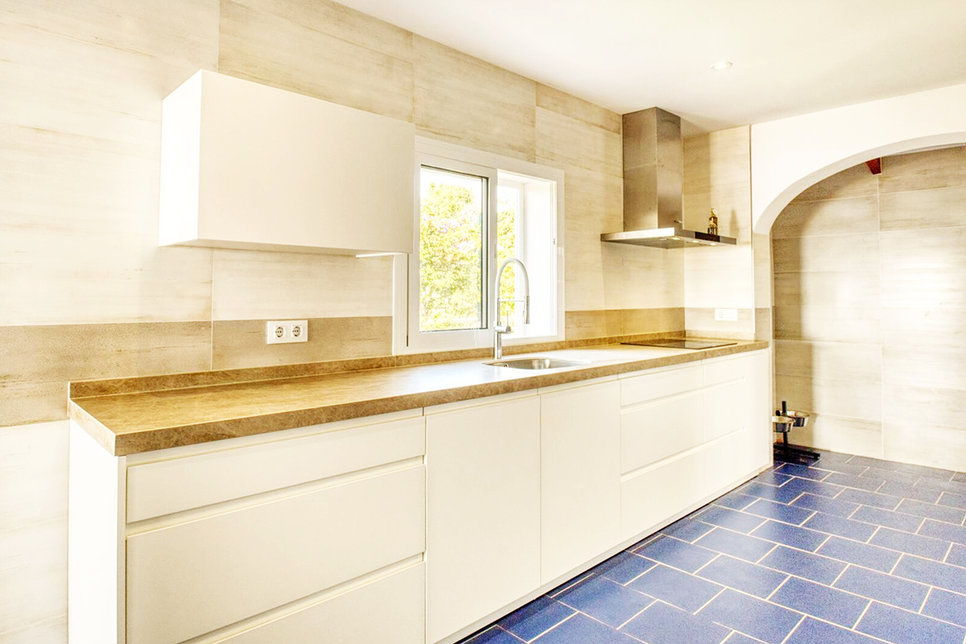 Sleek white kitchen with wooden countertops and built-in appliances featuring blue floor tiles.