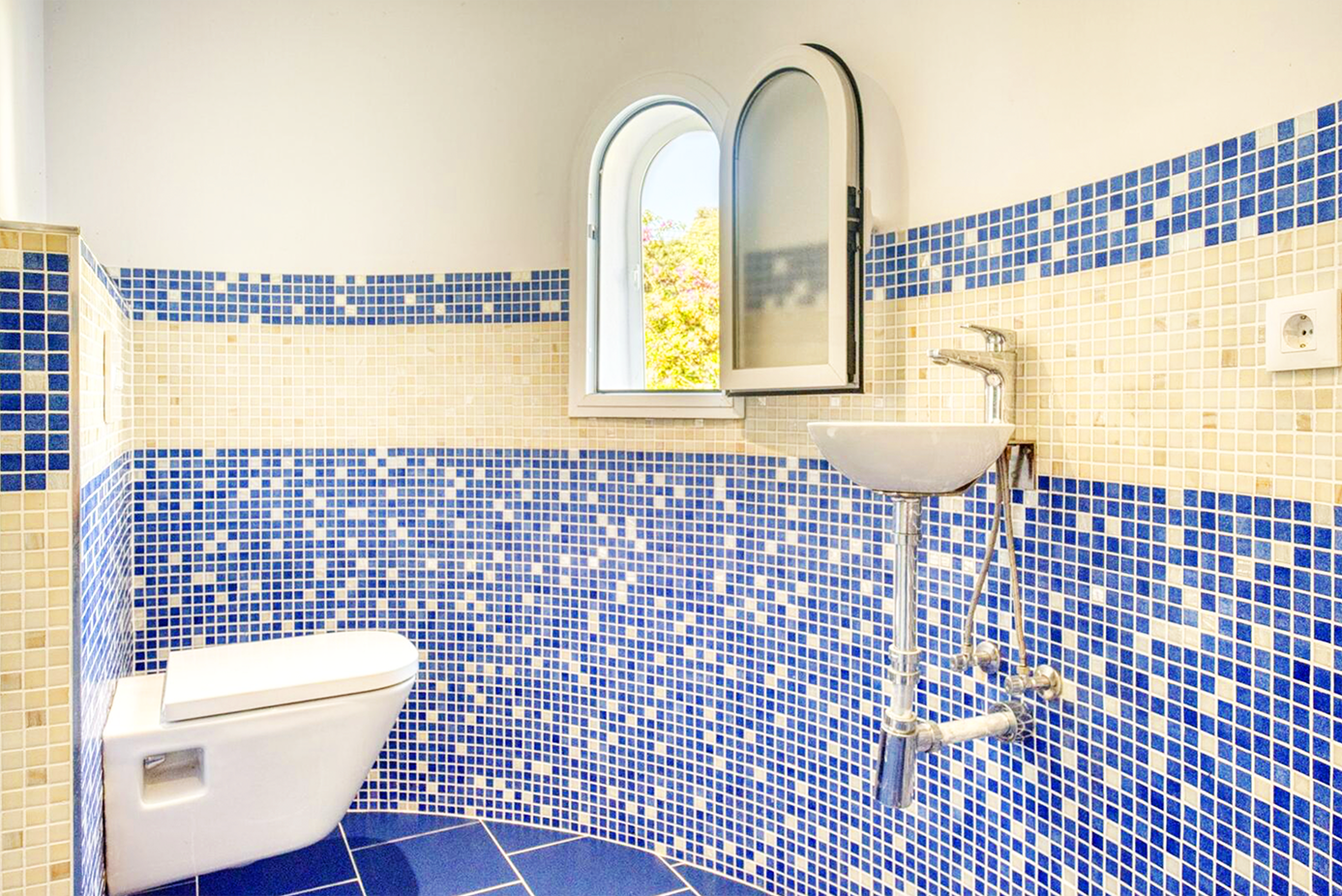 Bathroom with blue mosaic tile walls and modern fixtures featuring an arched mirror.