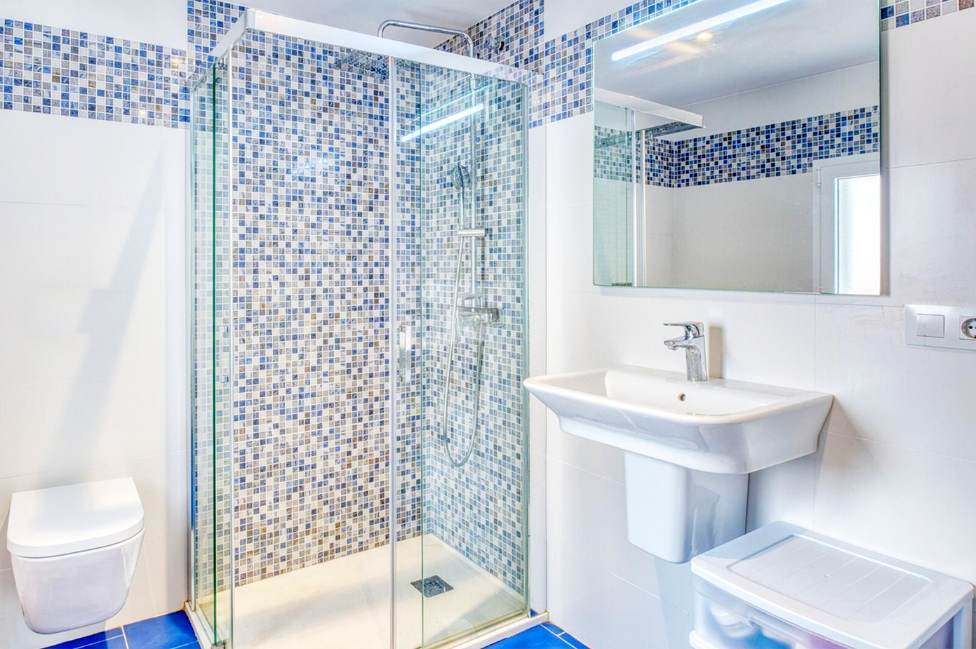Modern bathroom with blue mosaic tile shower enclosure and white fixtures.