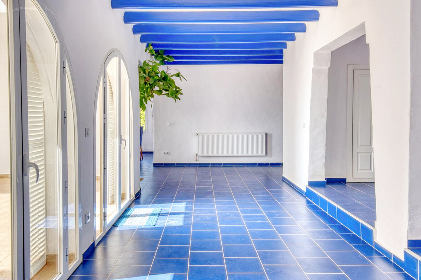 Mediterranean hallway with white walls, blue ceiling beams, and glossy blue floor tiles.