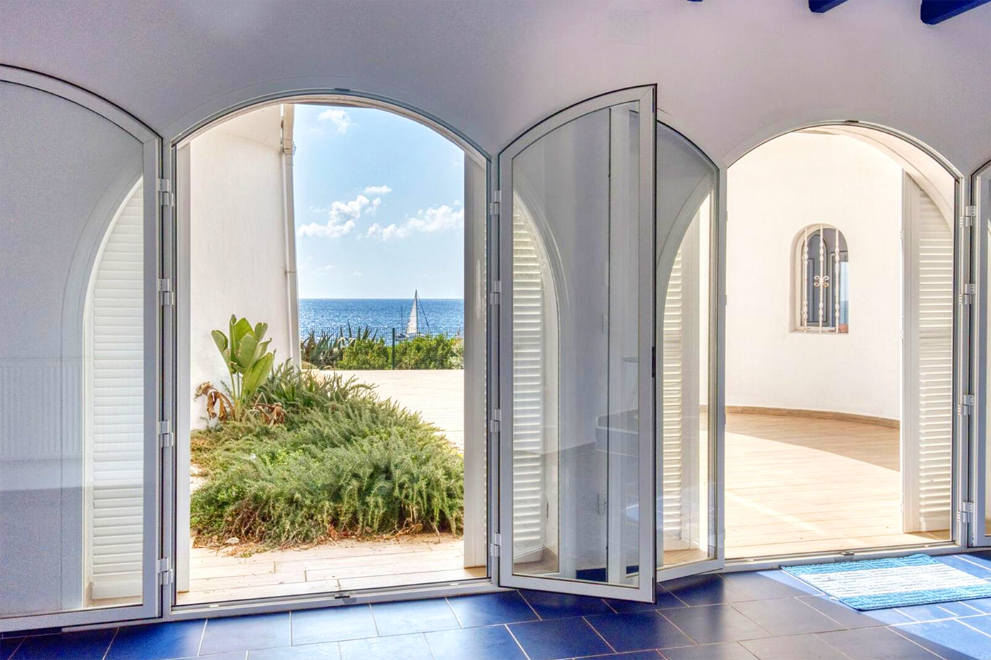 Arched doorways framing an ocean view with white shutters and blue tiled floor.