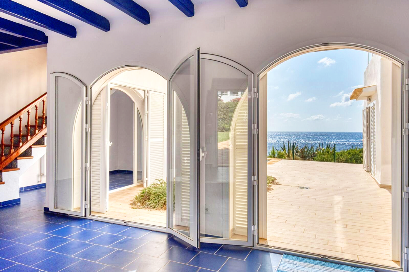 Coastal villa interior with arched doorways, blue floors, and stunning sea views.