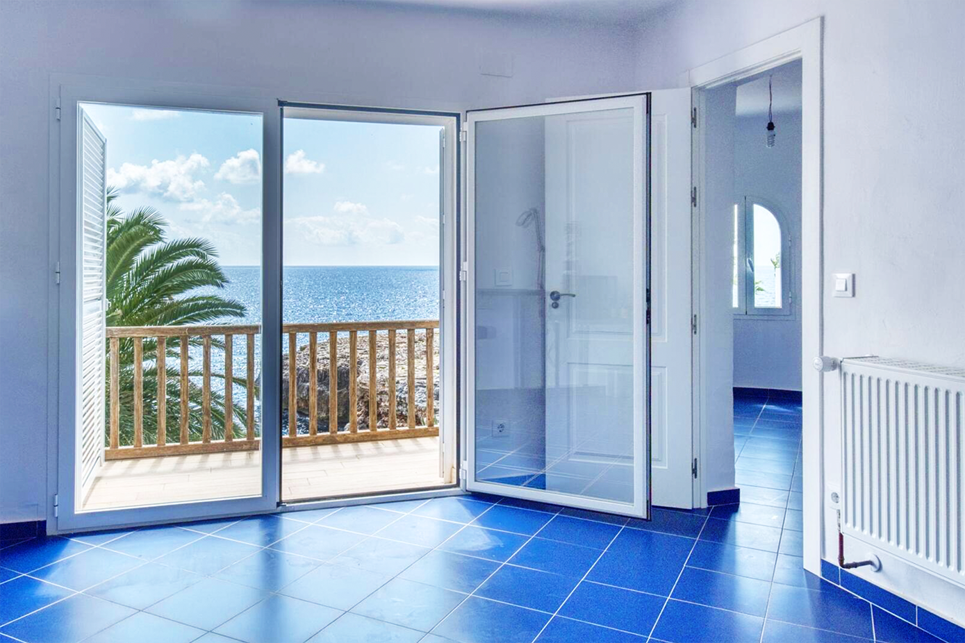 Room with blue floor tiles and French doors opening to a seaside balcony.