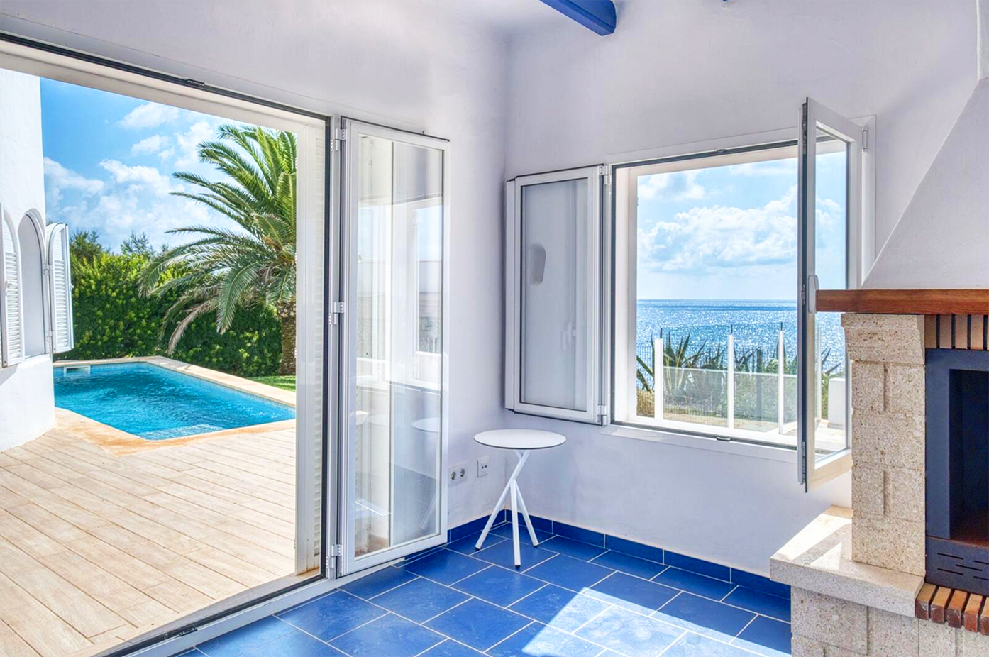 Bright coastal room with blue floors, white walls, and glass doors overlooking pool and ocean.