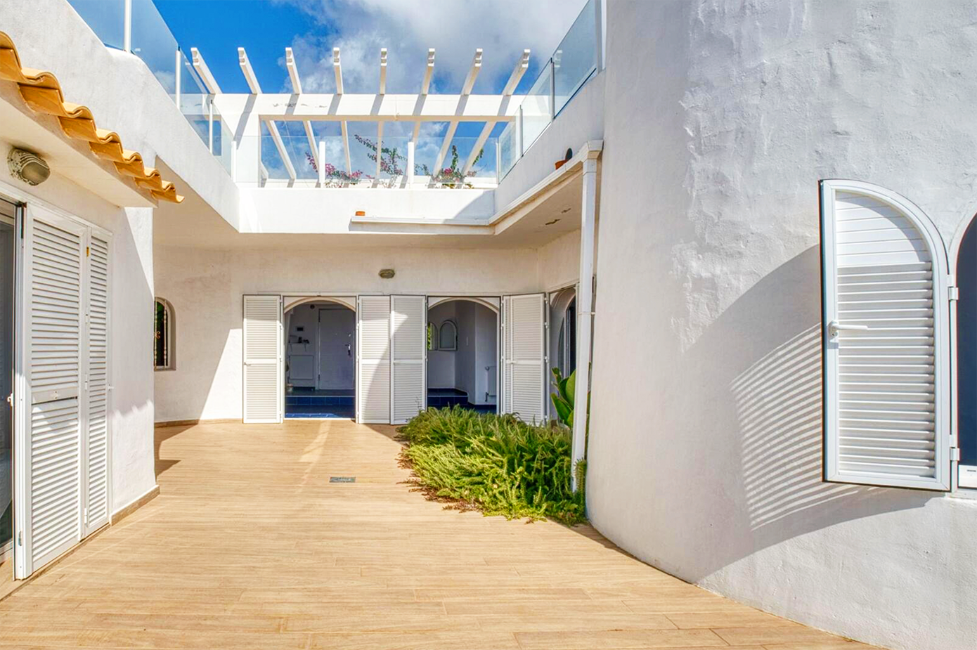 White Mediterranean courtyard with wooden pergola and blue shuttered doors.