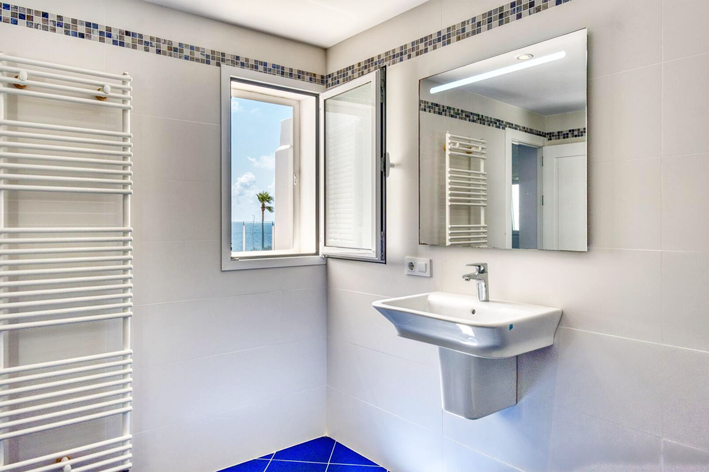 Modern white bathroom with heated towel rack, wall-mounted sink, and window.