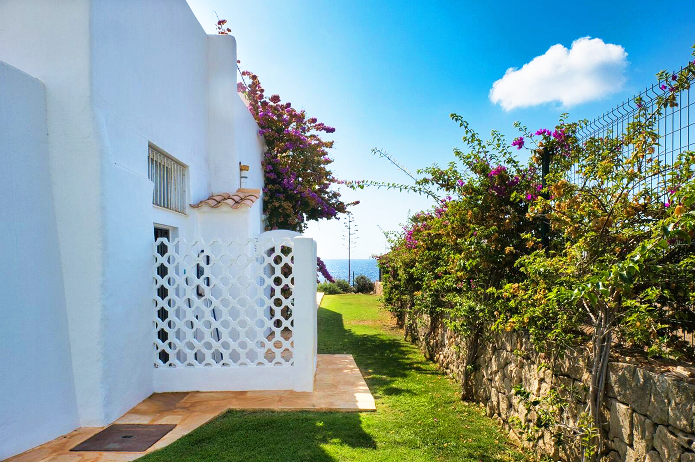 White Mediterranean villa exterior with lattice gate and flowering garden path.
