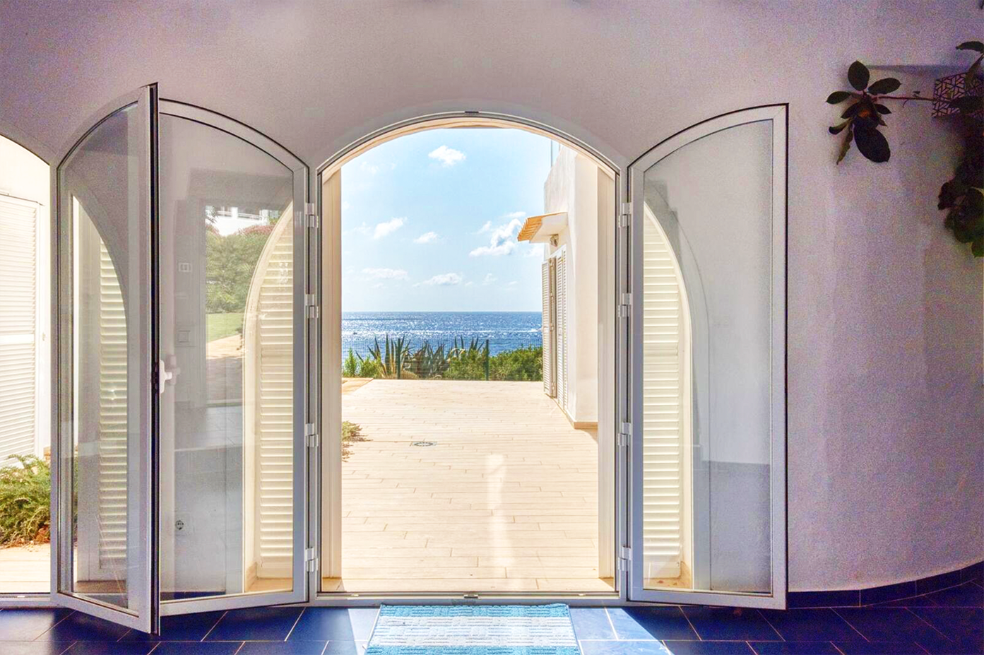 Arched doorway with white shutters framing a stunning ocean view beyond.