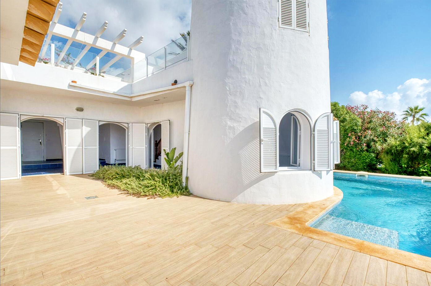 White villa exterior with curved architecture featuring a pool and wooden deck terrace.
