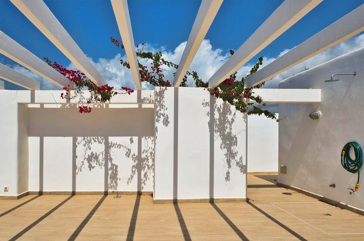 White pergola with climbing bougainvillea creating geometric shadows on terrace floor.