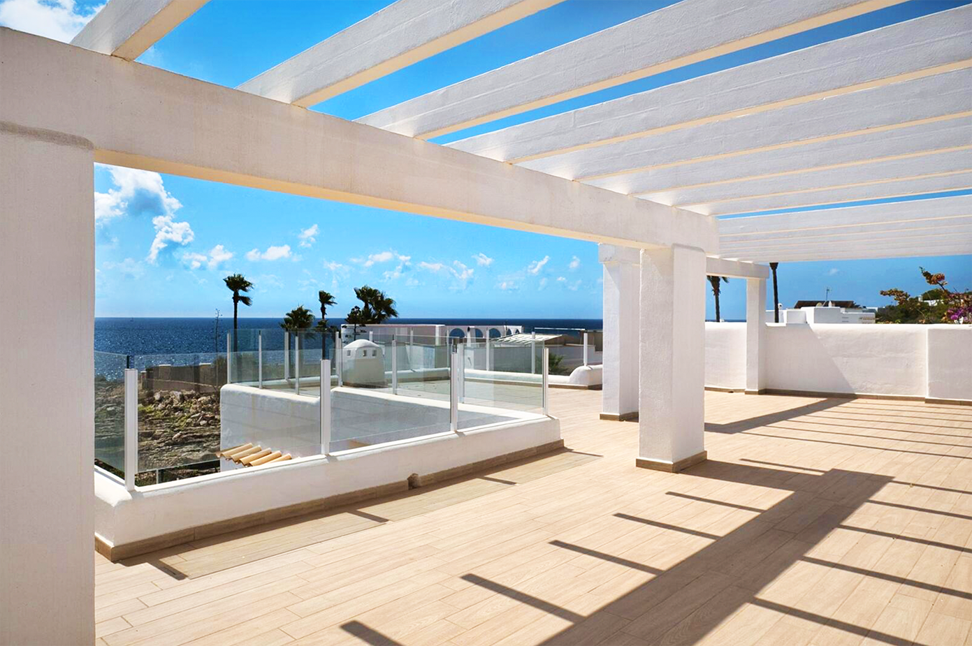 Modern white pergola terrace with ocean view and dramatic shadow patterns.