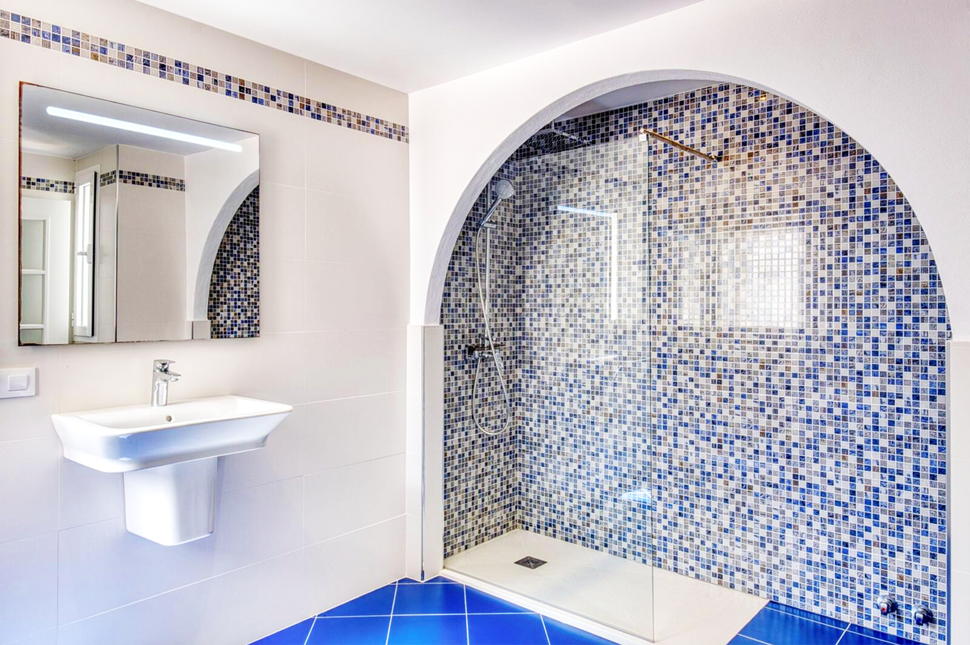 Modern bathroom with blue mosaic tile shower alcove and curved archway design.